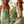 Vrouw in groene bloemenjurk en strohoed, lachend voor een raam. Zomerse mode, casual stijl, strandkleding, trendy dameskleding.