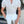 Man in gestreept wit overhemd en witte broek, staand voor een winkel. Modieuze herenkleding, casual zomeroutfit, stijlvolle uitstraling.