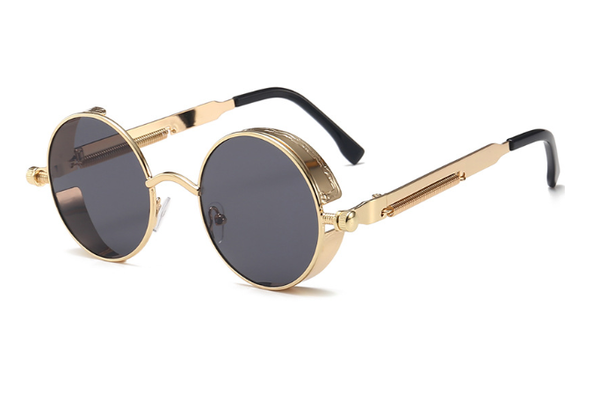 Gouden ronde zonnebril met donkere glazen en zwarte pootjes, retro stijl, unisex design, modieuze accessoire voor zomer en festivals.