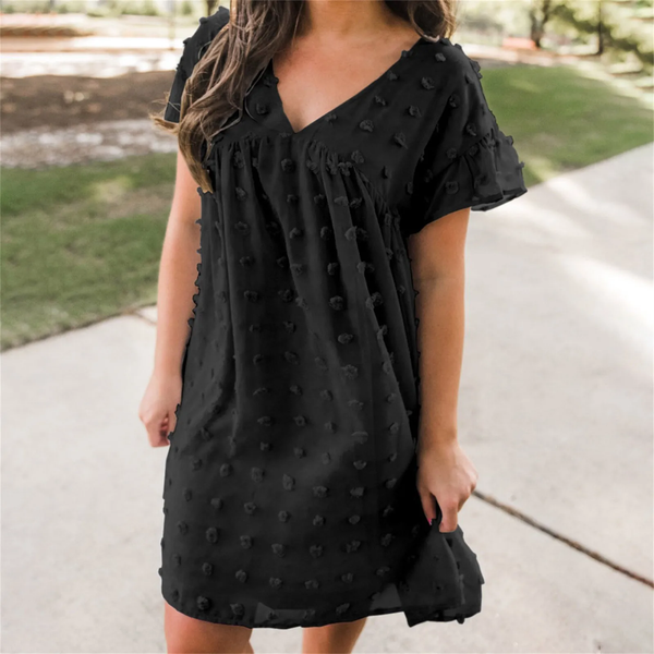 Vrouw in zwarte zomerjurk met stippenpatroon, buiten op een zonnige dag. Trendy damesmode, casual kleding, comfortabele outfit voor warm weer.