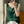 Vrouw in groene satijnen top en witte broek, poseert bij raam. Elegante mode, zomerse outfit, minimalistisch design, stijlvolle kleding.