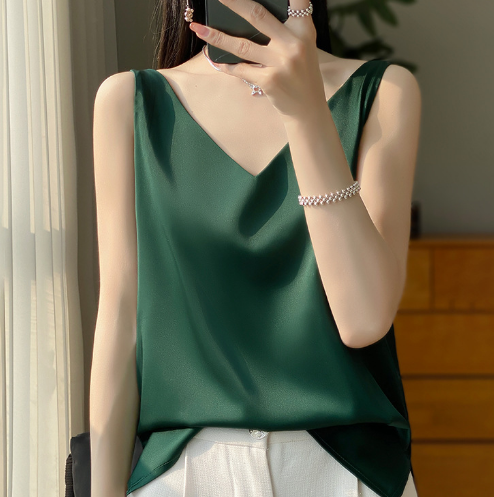 Vrouw in groene satijnen top en witte broek, poseert bij raam. Elegante mode, zomerse outfit, minimalistisch design, stijlvolle kleding.