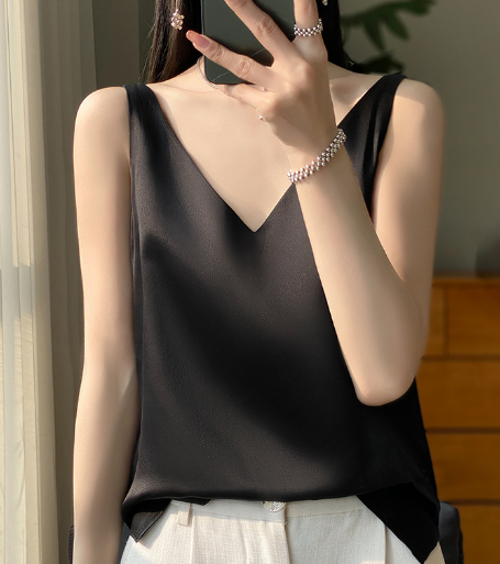 Zwarte satijnen top met V-hals, gedragen door vrouw, gecombineerd met witte broek. Elegante damesmode, minimalistisch design, zomerse outfit.