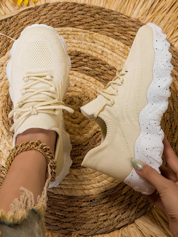 Beige sneakers met golvende witte zool, gedragen door persoon met gouden armband. Modieuze dames sneakers, casual stijl, comfortabele pasvorm.