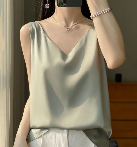 Vrouw in stijlvolle, lichtgroene satijnen top met V-hals, gecombineerd met witte broek. Elegante zomermode, perfect voor casual en chique gelegenheden.