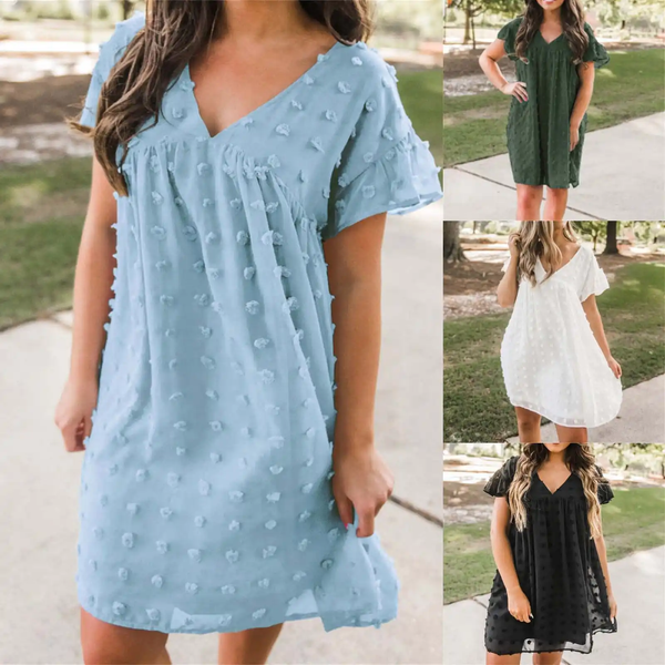 Vrouw in lichtblauwe zomerjurk met stippenpatroon, korte mouwen en V-hals. Drie extra kleuren: groen, wit en zwart. Perfect voor casual lente- en zomermode.