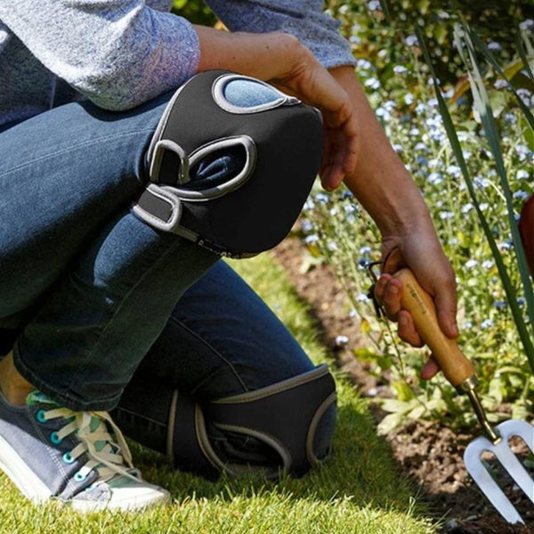 Tuinier met kniebeschermers en handgereedschap werkt in bloementuin. Tuinieren, kniebeschermers, handgereedschap, bloementuin, buitenwerk.