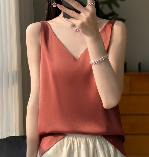 Vrouw in stijlvolle, mouwloze, terracotta top met V-hals, gecombineerd met lichte rok. Elegante sieraden, moderne mode, zomerse outfit.