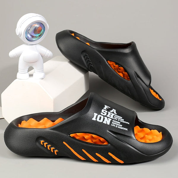 Zwarte en oranje unisex slippers met modern design en tekst "FASHION" op de zijkant, naast een decoratief astronautenbeeldje.