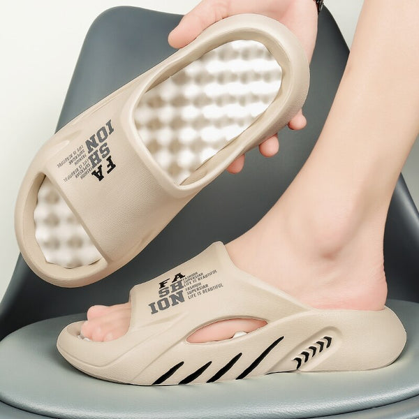 Beige slippers met dempende zool en tekst "FASHION" op de band, gedragen door een persoon op een grijze stoel. Comfortabele, modieuze slippers.