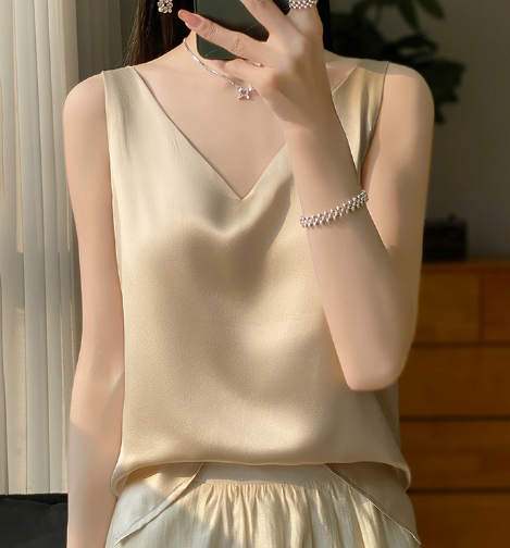 Zijdeachtige gouden top met V-hals, gedragen door vrouw, gecombineerd met parelarmband en ketting. Elegante damesmode, luxe kledingstijl.