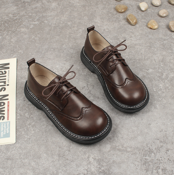 Bruine leren kinderschoenen met veters op grijze vloer, naast stenen en krant. Stijlvolle en duurzame schoenen voor dagelijks gebruik.