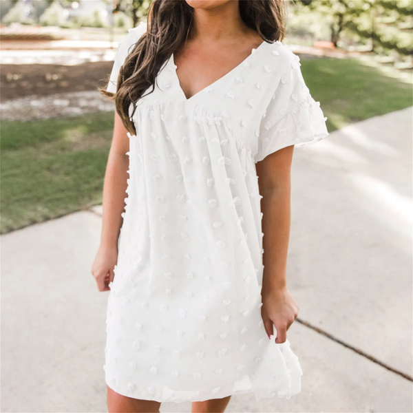 Vrouw in witte zomerjurk met stippenpatroon, buiten in zonnige omgeving. Perfecte casual outfit voor warme dagen. Zomerjurk, damesmode, casual stijl.