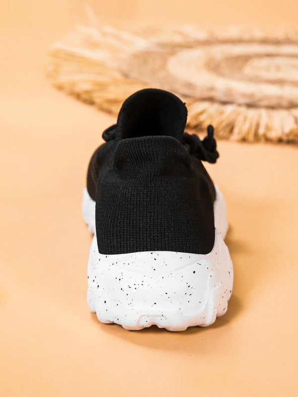 Zwarte sneaker met witte, gespikkelde zool op beige achtergrond. Moderne sportschoen, comfortabele pasvorm, trendy design, casual mode.