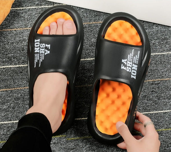 Zwarte slippers met oranje gewatteerde zolen, gedragen op een grijze tapijtachtergrond. Comfortabele mode-sandalen voor dagelijks gebruik.