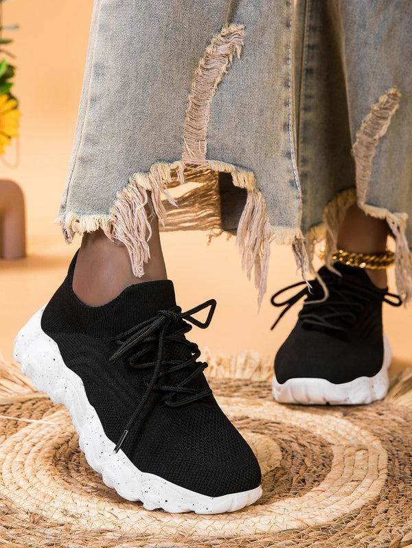 Zwarte gebreide sneakers met dikke witte zool, gedragen met gerafelde jeans. Trendy damesmode, comfortabele casual schoenen.