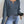 Vrouw in blauwe gebreide trui met V-hals en strakke jeans, houdt een wegwerpbeker vast. Modieuze herfstkleding, casual damesoutfit.