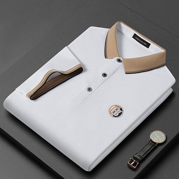 Opgevouwen witte polo met beige kraag en knopen, geborduurd logo op borst, naast een horloge. Luxe herenkleding, stijlvolle polo voor casual en formele gelegenheden.