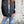 Vrouw in casual outfit met zwarte spijkerjas, witte top en blauwe jeans tegen een betonnen muur. Modieuze dameskleding, streetwear stijl.