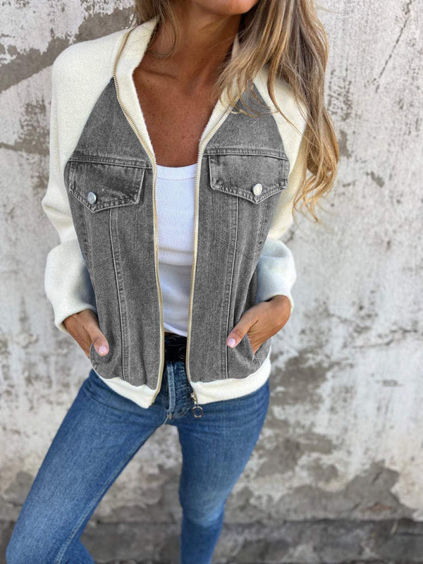 Vrouw draagt een stijlvolle jas met grijze denim accenten en witte mouwen, gecombineerd met een witte top en blauwe jeans, tegen een ruwe muur.