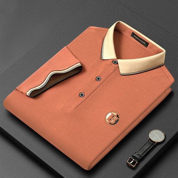 Oranje poloshirt met beige kraag, opgevouwen op zwarte achtergrond, naast een horloge. Stijlvolle herenkleding, casual mode, luxe uitstraling.
