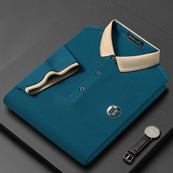 Opgevouwen blauwe poloshirt met beige kraag en knopen, naast een zwart leren horloge op een donkere achtergrond. Luxe herenkleding.