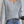 Grijze gebreide trui met V-hals, gedragen door vrouw met blauwe jeans, houdt een koffiebeker vast. Modieuze dameskleding, casual herfstoutfit.