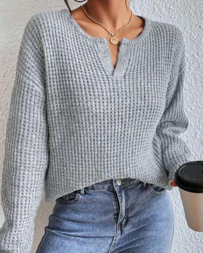 Grijze gebreide trui met V-hals, gedragen door vrouw met blauwe jeans, houdt een koffiebeker vast. Modieuze dameskleding, casual herfstoutfit.