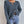 Donkergrijze gebreide trui met V-hals, gedragen door een vrouw, gecombineerd met lichtblauwe jeans. Modieuze dameskleding, herfststijl.
