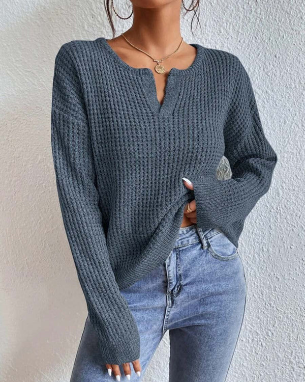 Donkergrijze gebreide trui met V-hals, gedragen door een vrouw, gecombineerd met lichtblauwe jeans. Modieuze dameskleding, herfststijl.
