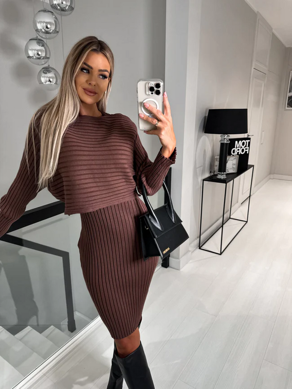 Vrouw in bruine geribbelde jurk maakt selfie, draagt zwarte tas en laarzen, moderne interieurachtergrond. Mode, herfstkleding, stijlvolle outfit.