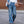 Vrouw in wijde blauwe spijkerbroek en witte blouse, draagt een blauwe tas. Modieuze casual outfit, trendy dameskleding, stedelijke stijl.