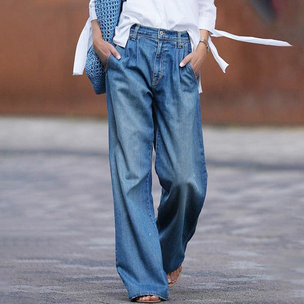 Vrouw in wijde blauwe spijkerbroek en witte blouse, draagt een blauwe tas. Modieuze casual outfit, trendy dameskleding, stedelijke stijl.