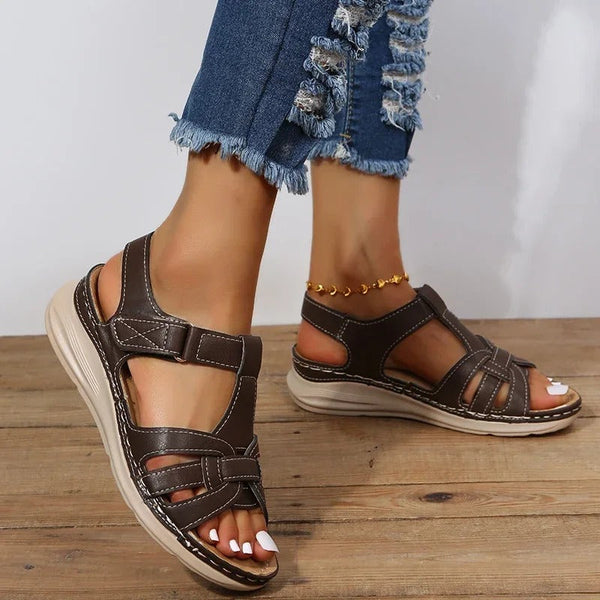 Bruine leren sandalen voor dames met klittenbandsluiting, gedragen met gescheurde jeans. Comfortabele zomerschoenen op houten vloer.