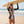 Vrouw in bloemen wetsuit draagt surfplank op strand. Zonnige dag, oceaan op achtergrond. Perfect voor surfen, strandmode, zomerse activiteiten.