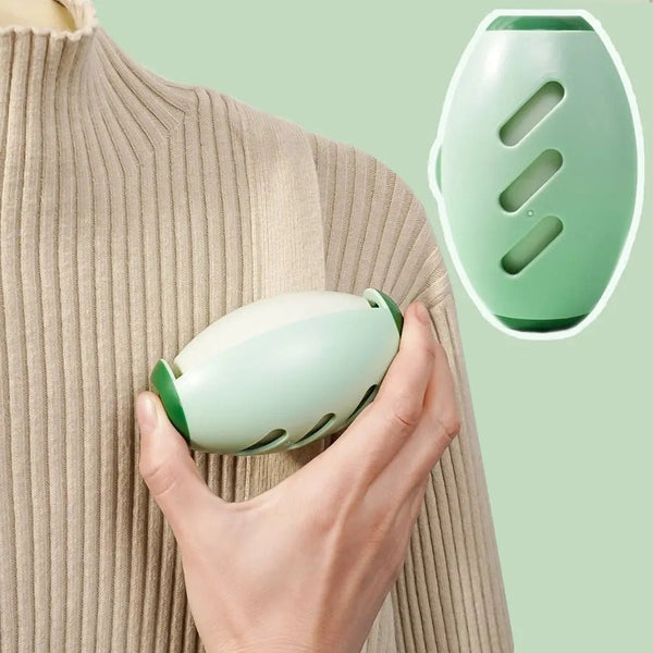 Hand houdt groene draagbare massageapparaat vast op beige trui; ergonomisch ontwerp, stressverlichting, spierontspanning, wellness gadget.