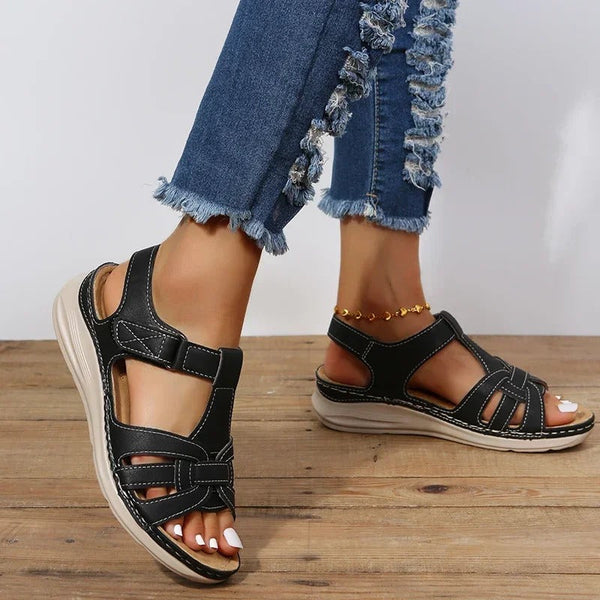 Zwarte dames sandalen met klittenband, comfortabele zool, gedragen met gerafelde jeans op houten vloer. Perfect voor casual zomeroutfits.