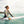 Vrouw in bloemen wetsuit op surfplank in oceaan, lachend, met golven en kustlijn op achtergrond. Surfen, watersport, strandvakantie.