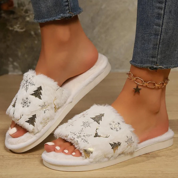 Witte pluche slippers met kerstboom- en sneeuwvlokmotief, gedragen door een persoon met jeans en een stervormige enkelband. Perfect voor wintermode.