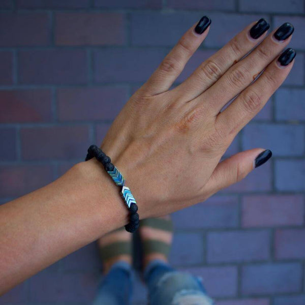 Hand met zwarte nagellak draagt een lavasteen armband met geometrische kralen, ideaal voor aromatherapie en etherische oliën.