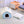 Blauw en wit hondenhuisje van pluche op een witte vloerkleed, naast een kussen en houten kastje. Perfect voor huisdierencomfort en interieurdecoratie.