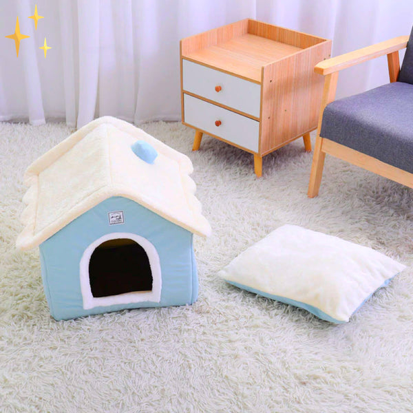 Blauw en wit hondenhuisje van pluche op een witte vloerkleed, naast een kussen en houten kastje. Perfect voor huisdierencomfort en interieurdecoratie.