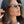 Vrouw met stijlvolle ronde zonnebril, goudkleurig montuur, modieuze kettingen, lang bruin haar, zomerse look. Perfect voor mode en accessoires SEO.