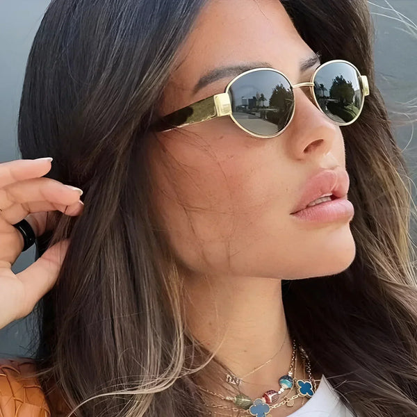 Vrouw met stijlvolle ronde zonnebril, goudkleurig montuur, modieuze kettingen, lang bruin haar, zomerse look. Perfect voor mode en accessoires SEO.