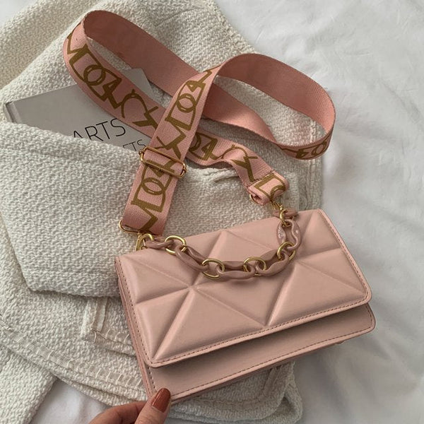 Lichtroze handtas met gewatteerd patroon en gouden kettingriem, op een witte stoffen achtergrond. Trendy damesmodeaccessoire.