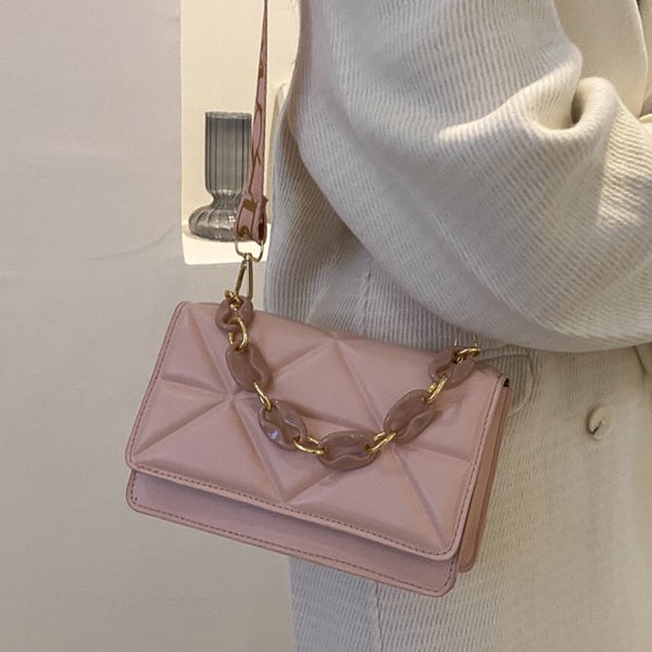 Roze handtas met gouden ketting en geometrisch patroon, gedragen door persoon in witte trui. Stijlvolle damesmodeaccessoire, trendy en elegant.