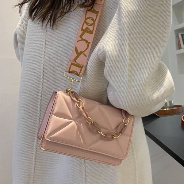Roze leren schoudertas met gouden ketting en verstelbare band, gedragen door vrouw in witte trui. Stijlvolle damesaccessoire, modieuze handtas.