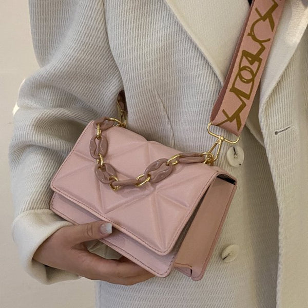 Vrouw met roze handtas met gouden ketting en brede schouderriem, gedragen over een witte jas. Stijlvolle modeaccessoire voor dames.
