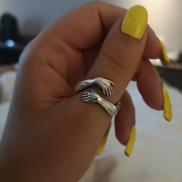 Zilveren ring met armenontwerp om vinger, gedragen door hand met gele nagellak. Unieke sieradenstijl, handgemaakt, modieuze accessoire.