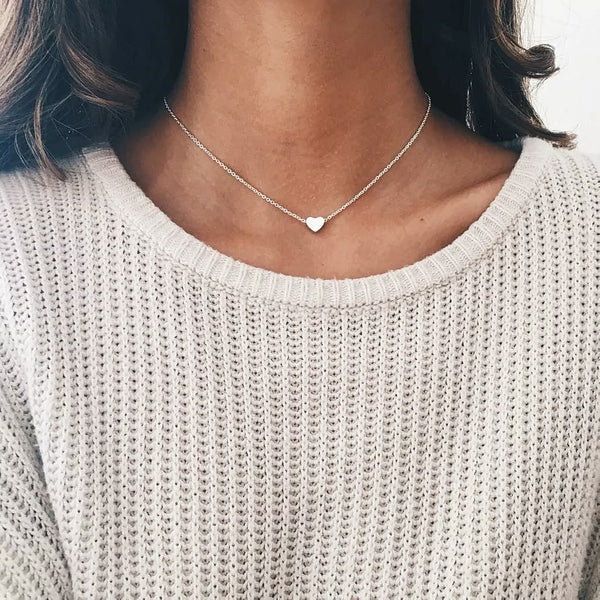 Vrouw met zilveren hartvormige ketting, gebreide trui, minimalistische sieraden, modieuze accessoires, elegante damesstijl, casual outfit.